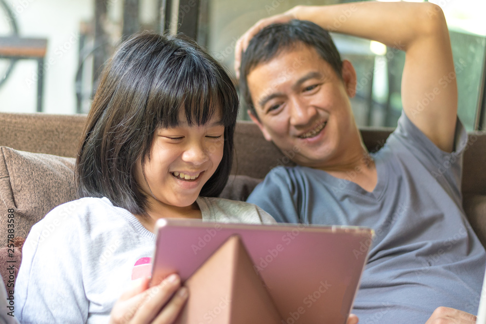 Father and daughter concept. Daddy working on computer notebook hand typing on keyboard while Asia kid girl using tablet hand touching on touchscreen playing game. Father and daughter concept. Daddy working on computer notebook hand typing on keyboard while Asia kid girl using tablet hand touching on touchscreen playing game.