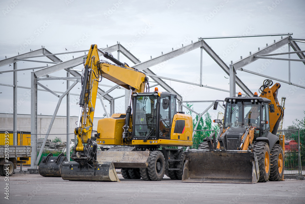 Multiple cars, excavators, trucks, loaders, concrete mixers and construction machinery in large parking lot in industrial territory, next to concrete and asphalt factory  
