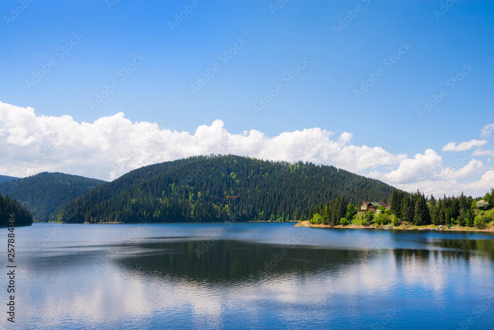 Beautiful mountain landscape with lake and reflections in water in summer. Tiny house or hotel on side of river. Concept of traveling. Clean environment. 