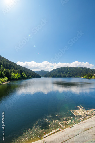 Polluted, toxic river at hydroelectric dam in Romania, Cluj Napoca. Beautiful mountain landscape with lake and reflections in water in summer. Garbage all around. Concept of environment protection