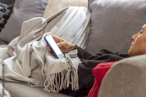 woman on a couch under a blanket using a cell phone