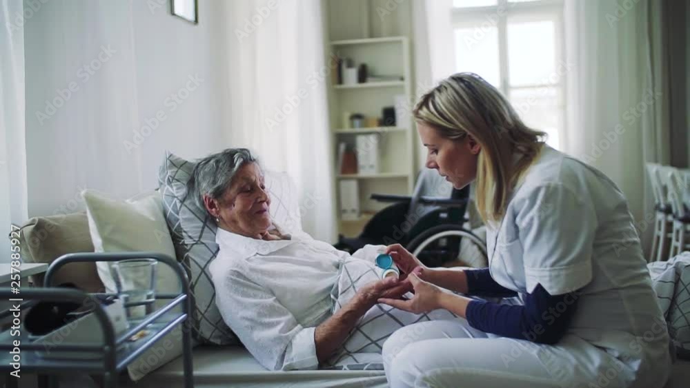 A health visitor giving pills to a sick senior woman lying in bed at home. A health visitor giving pills to a sick senior woman lying in bed at home.