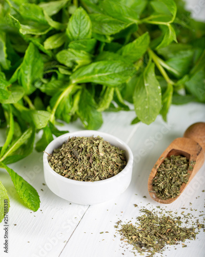 Dried peppermint in a white bowl and a bunch of fresh mint, on wooden background. Food background.