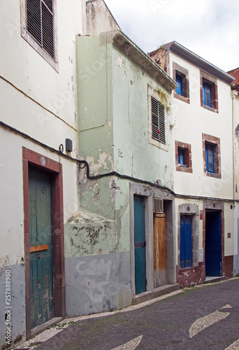 a typical quiet empty street in funchal madeira with old traditional houses painted in faded pastel peeling paint and a cobbled road © Philip J Openshaw 