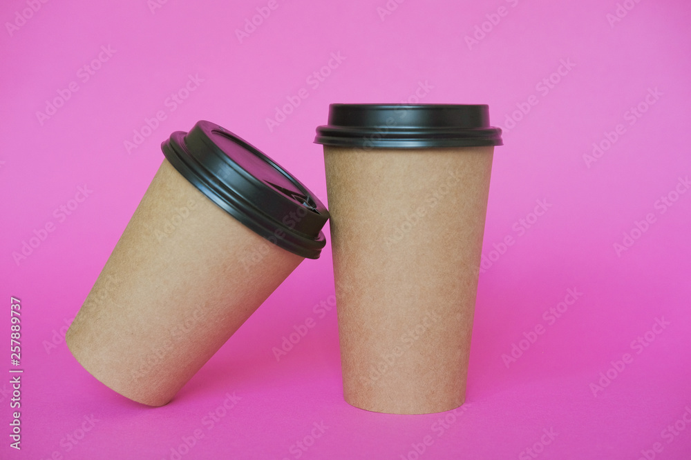 Coffee cup on pink paper background. A couple of paper cups of coffee to take away.