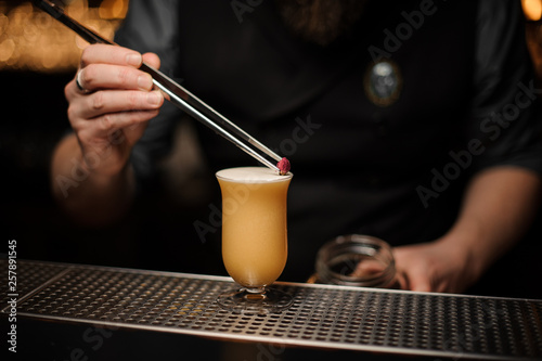 Professional bartender adding to a delicious cocktail decor of the little rose bud with tweezers