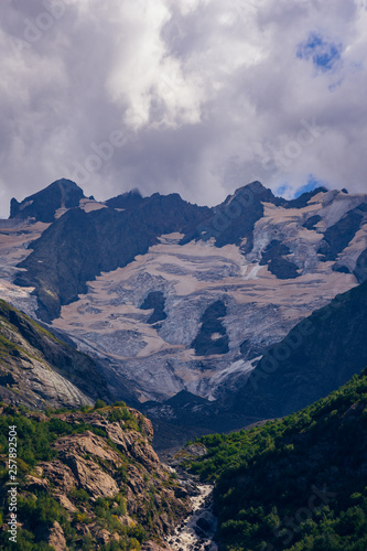 Massive peaks of the Caucasus Mountains in the snow in the surroundings of dombai in the clouds. Summer day.