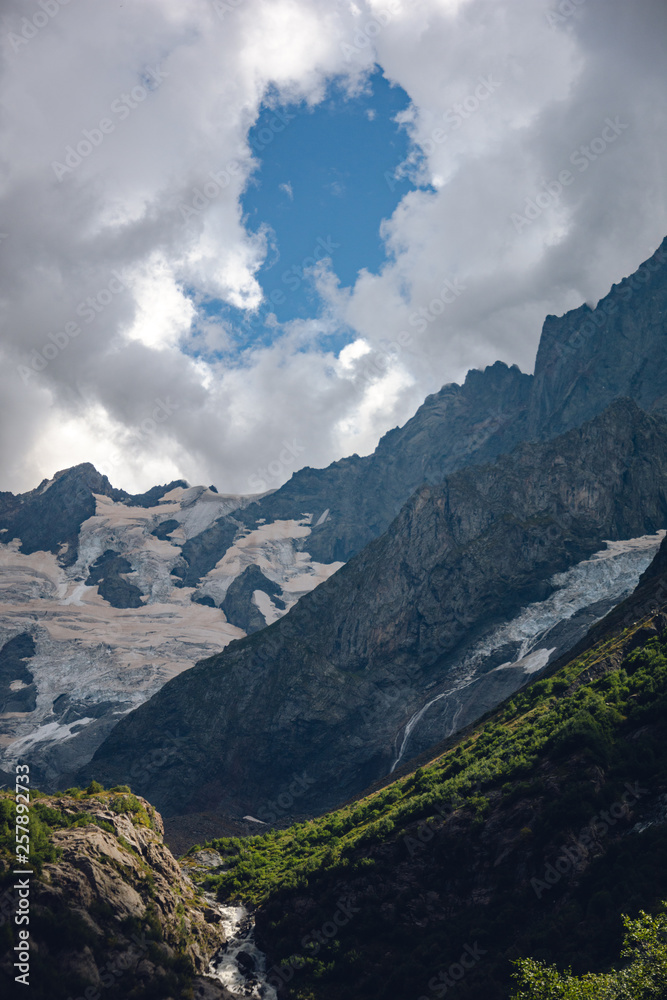 Massive peaks of the Caucasus Mountains in the snow in the surroundings of dombai in the clouds. Summer day.