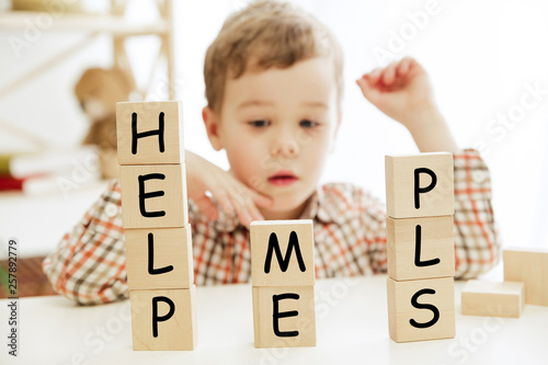 Photos Wooden cubes with words HELP ME PLS in hands of little boy at home