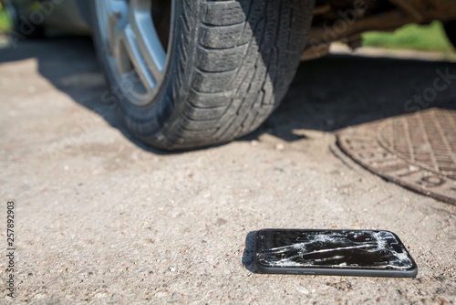 Broken and damaged smartphone with cracks on glass screen laying on ground. Accident. Cell phone under car wheel. Concept of warranty and lost smartphone 