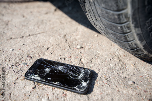 Broken and damaged smartphone with cracks on glass screen laying on ground. Accident. Cell phone under car wheel. Concept of warranty and lost smartphone 