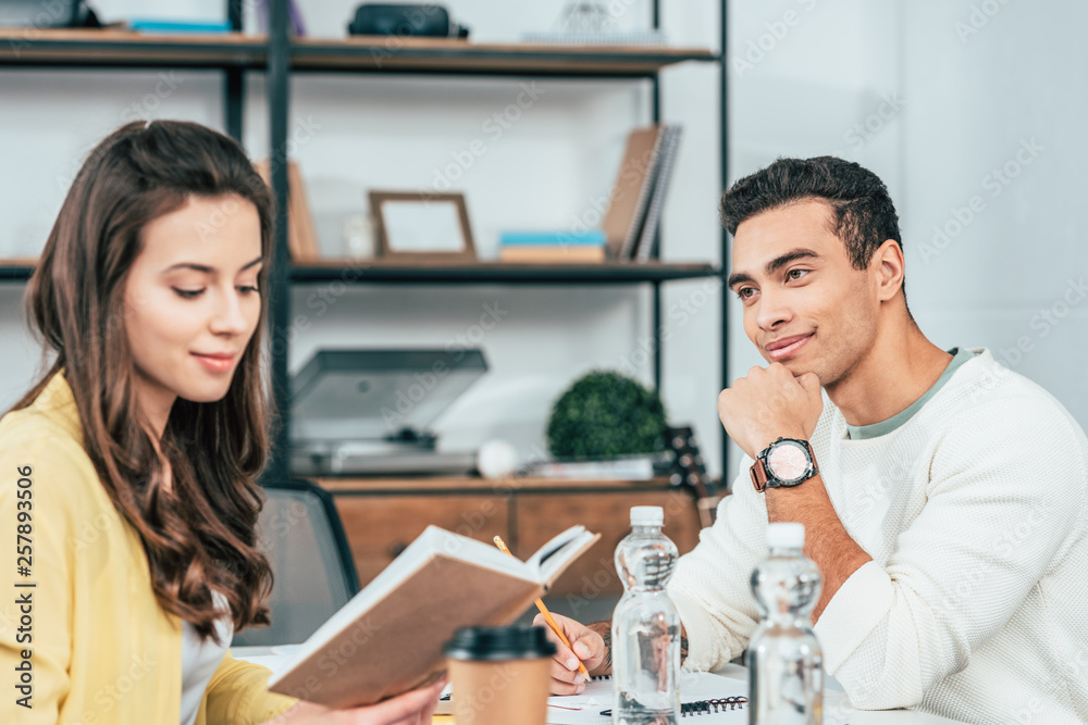 Two multiethnic students sitting at desk with books and studying together Two multiethnic students sitting at desk with books and studying together