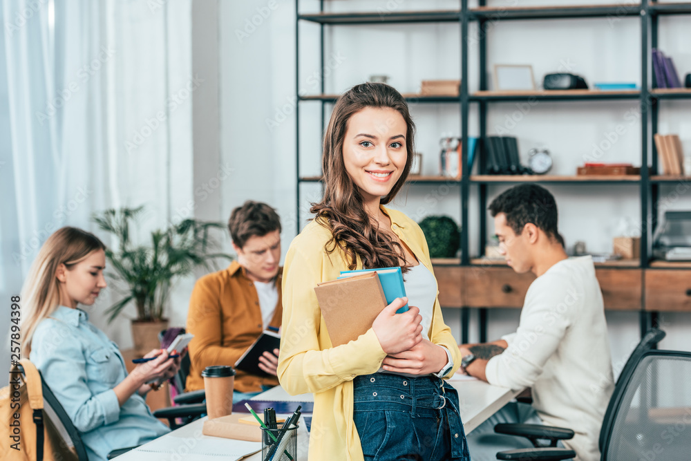 Obraz premium Charming smiling student standing near table and holding books