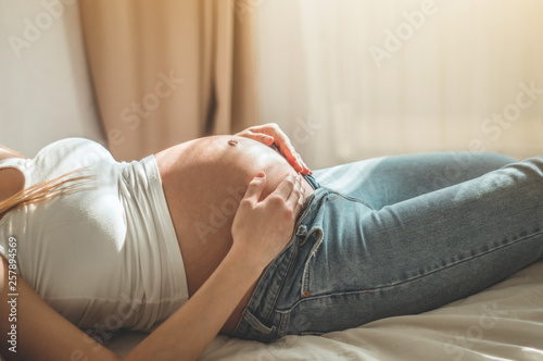 Beautiful pregnant woman is lying on the bed and holding herself by the belly. Relaxation