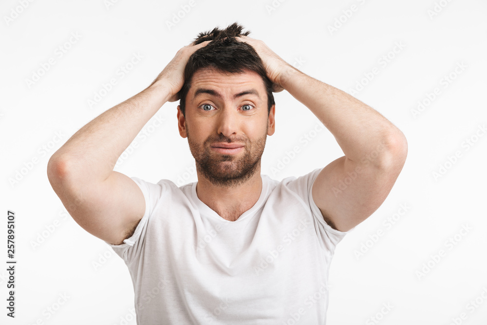 Image of brunette man 30s with bristle in casual t-shirt frowning and grabbing head Image of brunette man 30s with bristle in casual t-shirt frowning and grabbing head