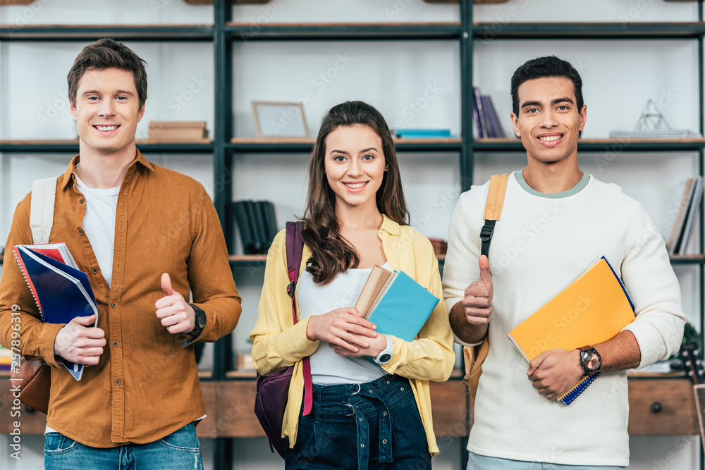 Three multiethnic happy students holding notebooks and showing thumbs up Three multiethnic happy students holding notebooks and showing thumbs up