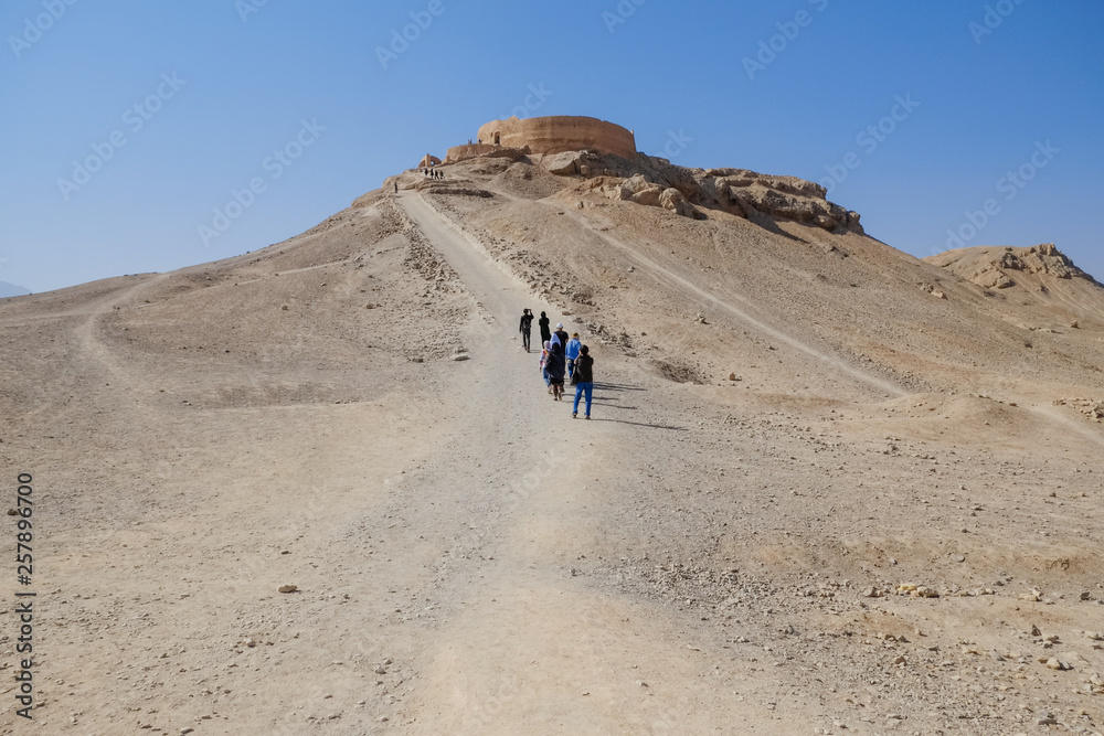 Tourists walking to the ancient buildings of Zoroastrian Dakhma. Persian tower of silence. Yazd, Iran.