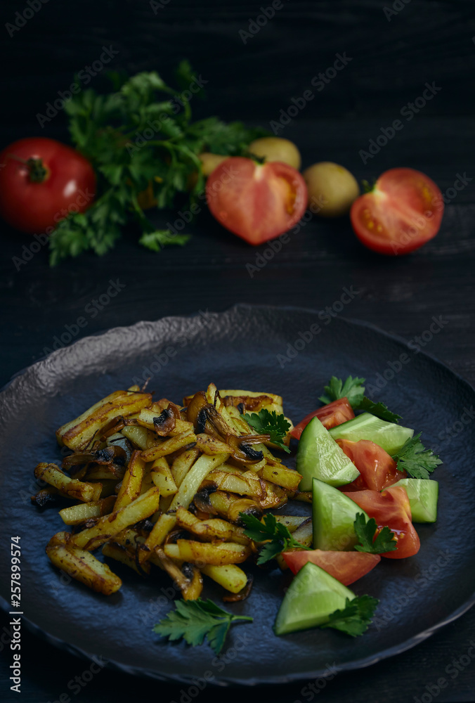 Freshly cooked fried potatoes with onions and mushrooms close-up on a plate. ebony table. vertical view of the dish. Freshly cooked fried potatoes with onions and mushrooms close-up on a plate. ebony table. vertical view of the dish.