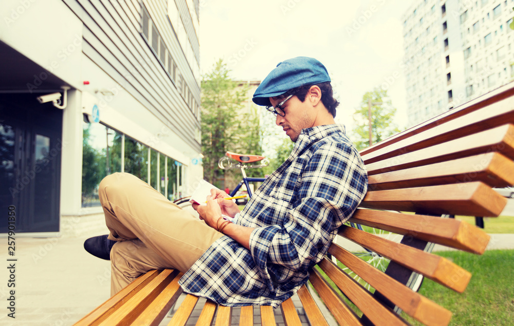 lifestyle, creativity, freelance, inspiration and people concept - creative man with notebook or diary writing sitting on city street bench