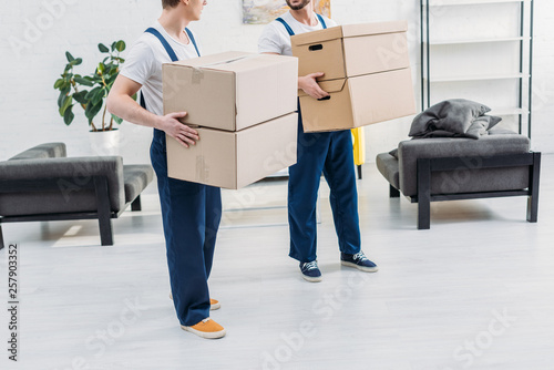 cropped view of two movers in uniform carrying cardboard boxes in apartment