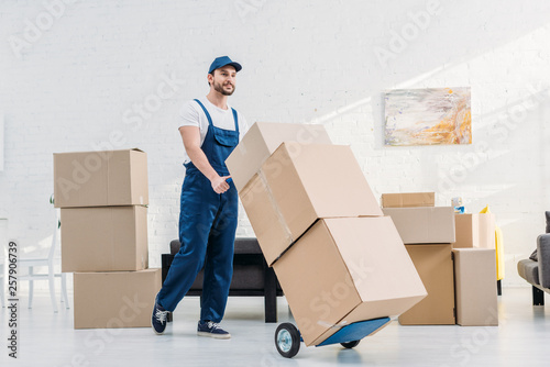 mover in uniform transporting  cardboard boxes on hand truck in apartment photo