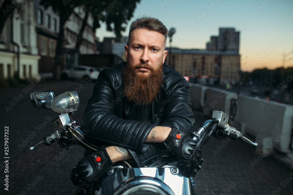 Brutal bearded biker poses on chopper, front view