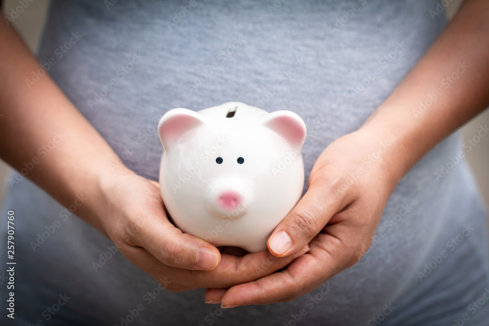 Women is pregnant hold a pig bank in the public park, a saving money for future investment concept. Women is pregnant hold a pig bank in the public park, a saving money for future investment concept.