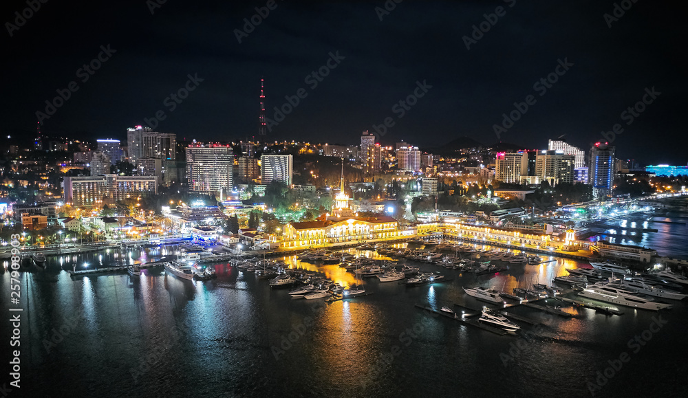 Obraz premium Sochi sea port. Aerial drone. Berth for marine yachts and boats. The historic building of the seaport. Evening illumination of the city.