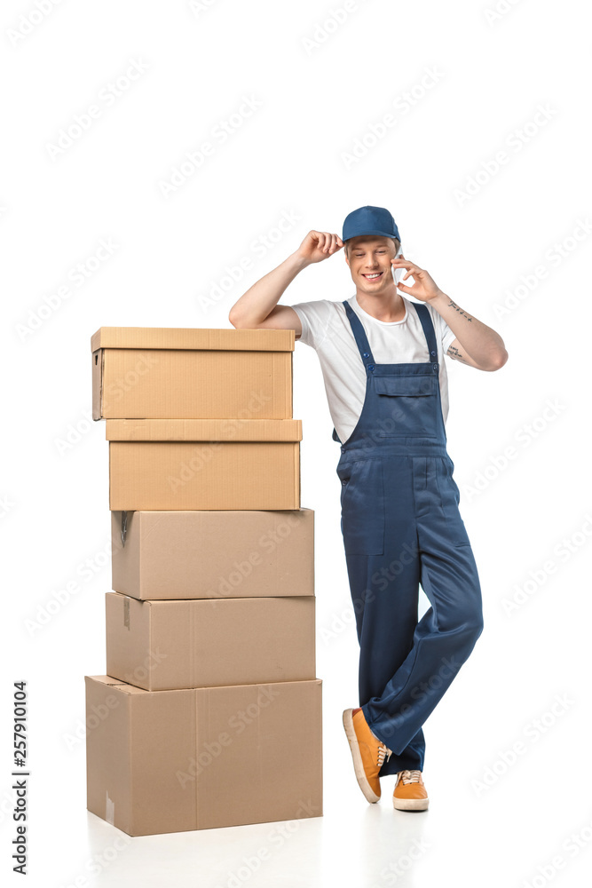 handsome smiling mover in uniform with cardboard boxes talking on smartphone isolated on white handsome smiling mover in uniform with cardboard boxes talking on smartphone isolated on white