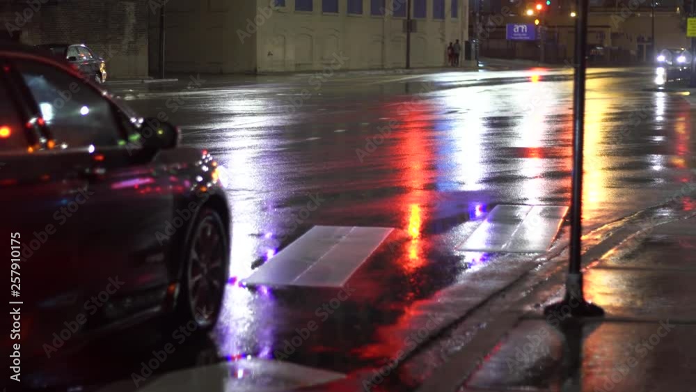 Chicago Illinois/United States March 24th 2019:  person walking in the middle of the night after a light rain as the street lights illuminate the concrete pavement. the car passing by driving home.