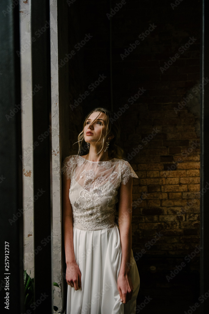 Model posing in a white long wedding dress indoors by the window. Advertising of wedding dresses