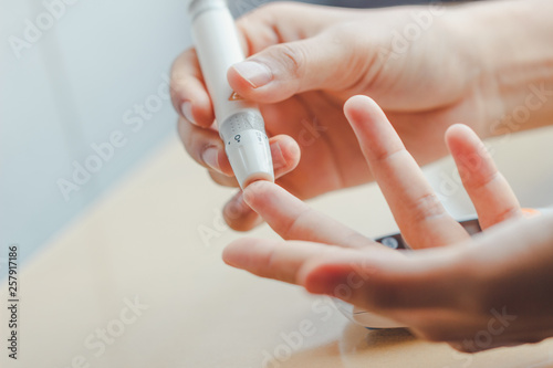 Close up of woman hands using lancet on finger to check blood sugar level by Glucose meter using as Medicine, diabetes, glycemia, health care and people concept.