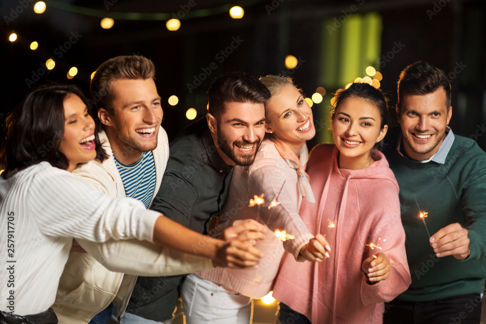 Fototapeta premium leisure, celebration and people concept - happy friends with sparklers at rooftop party at night