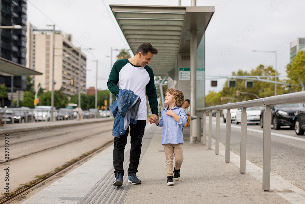 Smiling father and son walking hand in hand at tram stop in the city Smiling father and son walking hand in hand at tram stop in the city