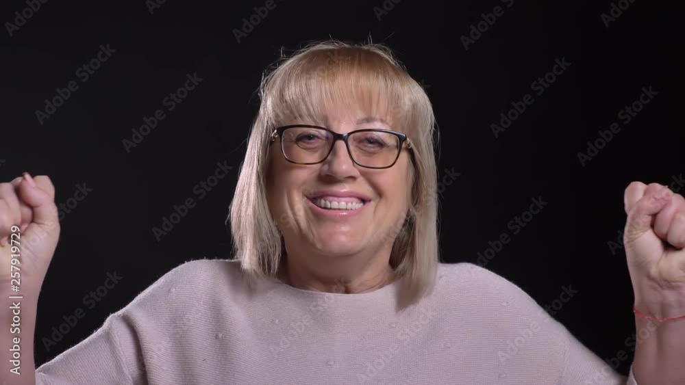 Closeup shoot of senior caucasian blonde female in glasses getting excited and celebrating in front of the camera with background isolated on black Closeup shoot of senior caucasian blonde female in glasses getting excited and celebrating in front of the camera with background isolated on black