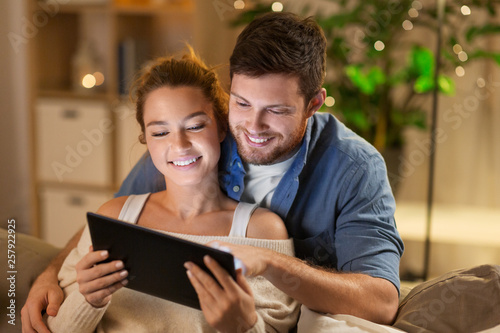 technology, internet and people concept - happy couple using tablet computer at home in evening