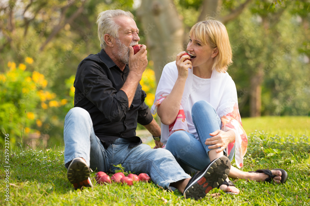 Fototapeta premium Happy senior couple relaxing in park eating apple together morning time. old people sitting on grass in the autumn park . Elderly resting .mature relationships. family