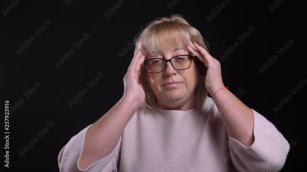 Closeup shoot of senior caucasian blonde female in glasses having a headache and being tired with background isolated on black Closeup shoot of senior caucasian blonde female in glasses having a headache and being tired with background isolated on black