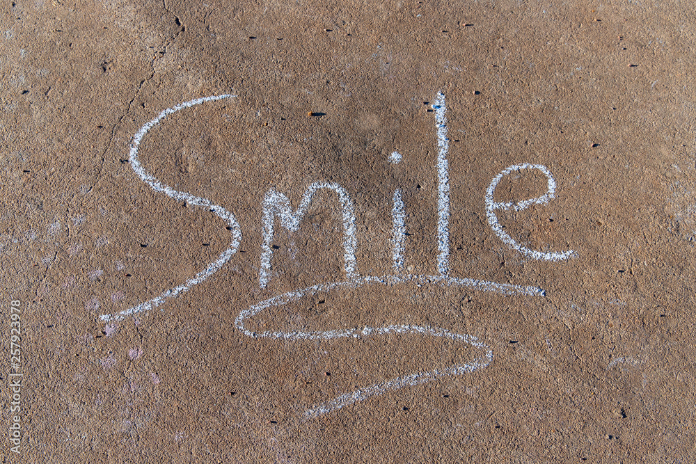 Fototapeta premium the word Smile written with sidewalk chalk on gray concrete background