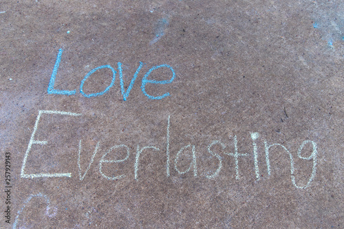 the words Love everlasting written with sidewalk chalk on gray concrete pavement background