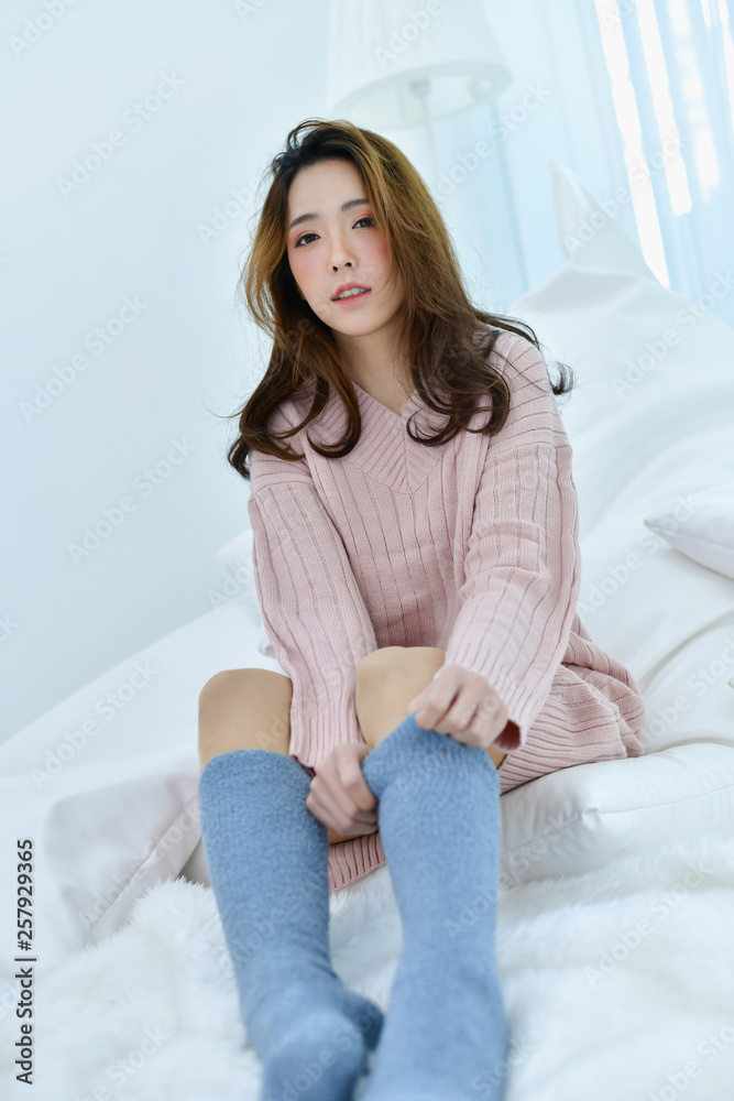 Winter Concept. Beautiful woman is relaxing in bedroom. Woman wearing a sweater in white bedroom. Winter Concept. Beautiful woman is relaxing in bedroom. Woman wearing a sweater in white bedroom.