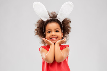 childhood, party props and easter concept - happy little african american girl wearing bunny ears headband posing over grey background