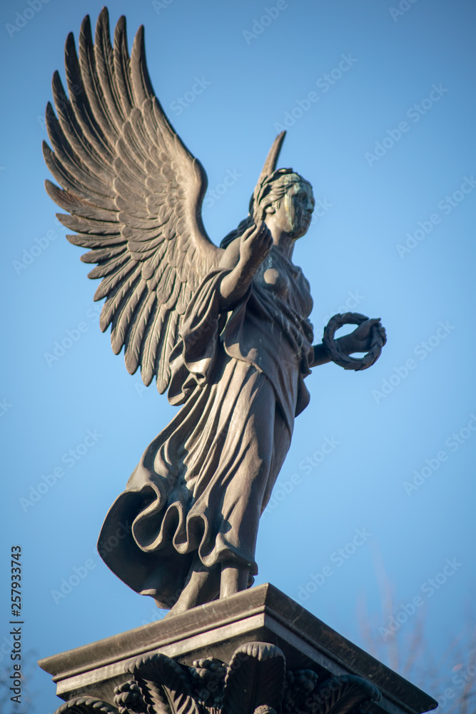 Fototapeta premium Engel Statue auf Podest mit Lorbeerkranz auf dem Dorotheenstädtischen Friedhof in Berlin