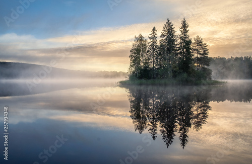 Scenic lake view with sunrise, island and foggy mood at beautiful autumn morning in Finland
