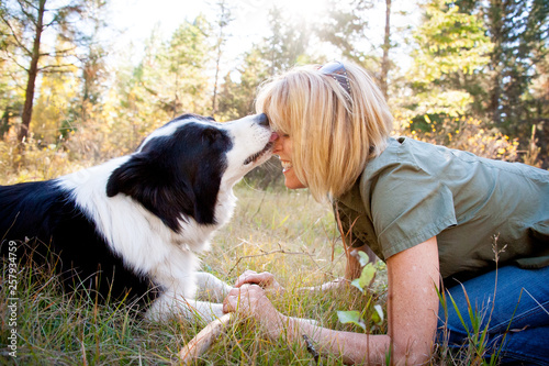 Dog licking woman's nose while sitting on grassy landscape