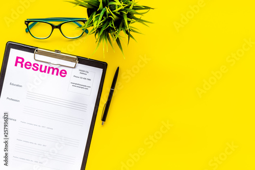 Empoyment concept with resume on yellow work desk background with pen, glasses top view space for text photo