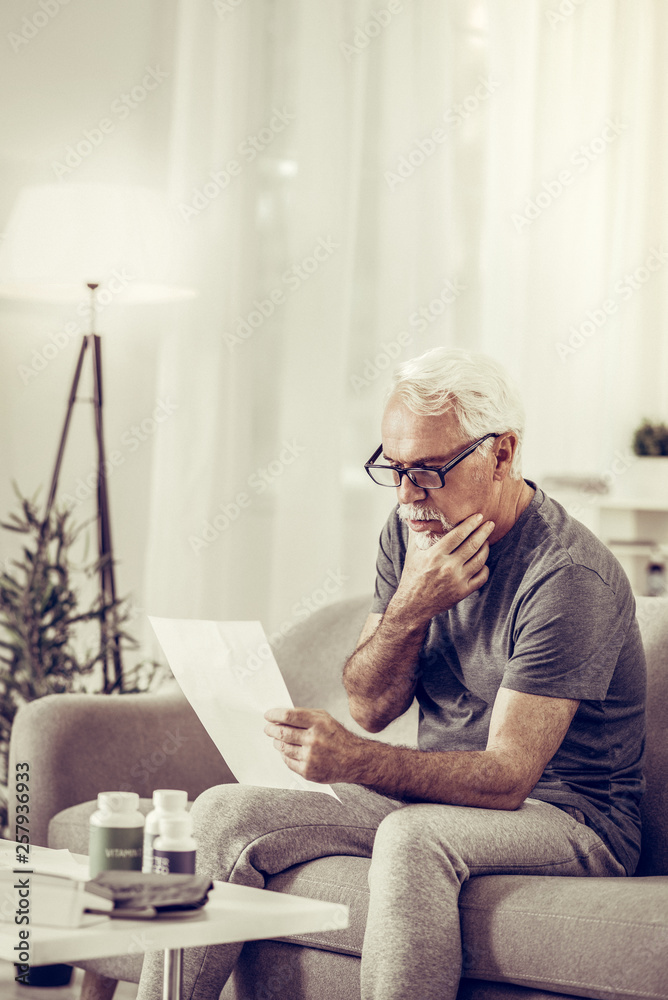 Aged handsome gentleman carefully considering documents that holding in hands