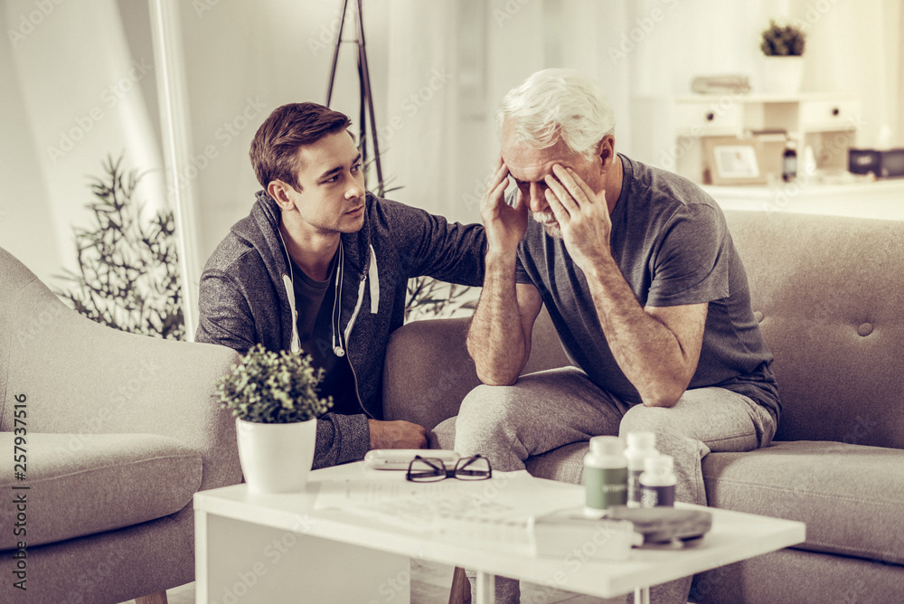 Young dark-haired pleasant son calming down aging silver-haired devastated father
