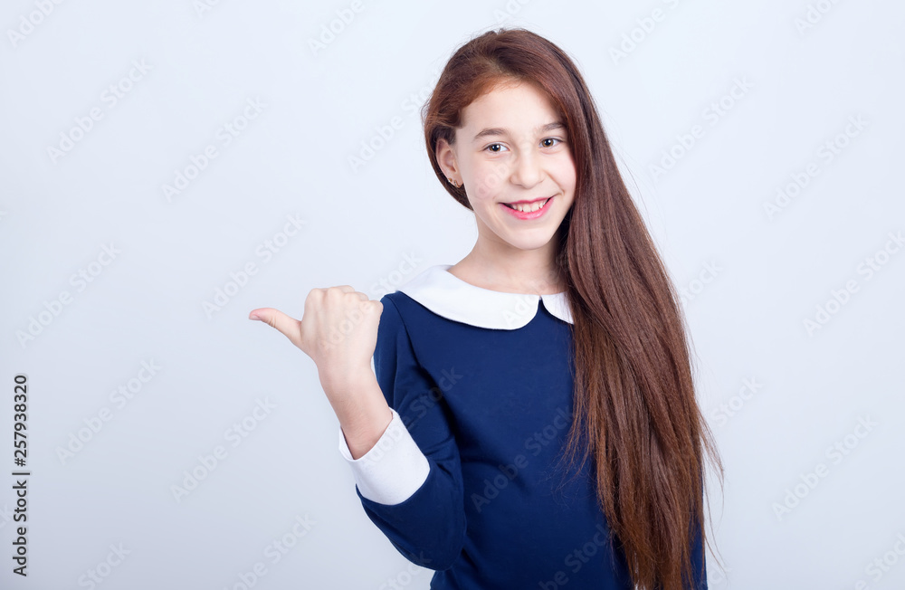 Portrait of a smiling girl pointing her finger to the side on a light background. Schoolgirl. Portrait of a smiling girl pointing her finger to the side on a light background. Schoolgirl.