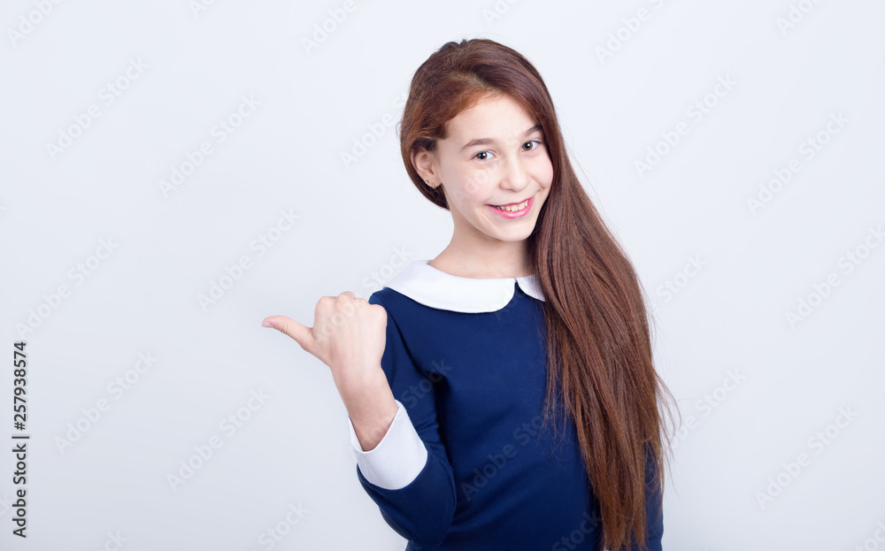 Portrait of a smiling girl pointing her finger to the side on a light background. Schoolgirl. Portrait of a smiling girl pointing her finger to the side on a light background. Schoolgirl.